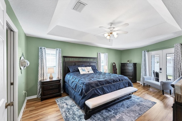 bedroom featuring french doors, light hardwood / wood-style floors, ceiling fan, and a tray ceiling