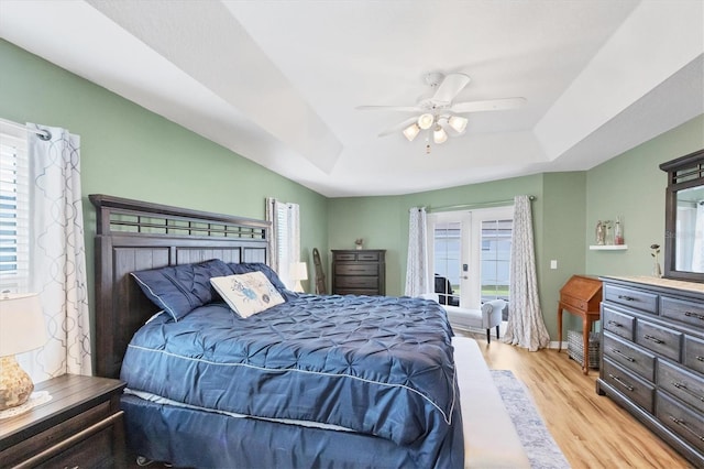 bedroom with access to exterior, light hardwood / wood-style flooring, ceiling fan, and a raised ceiling