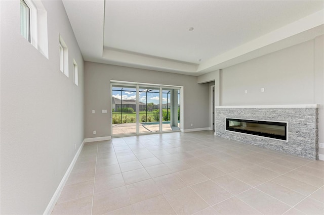 unfurnished living room with a stone fireplace, light tile patterned floors, and a raised ceiling