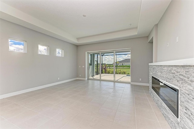 unfurnished living room with a fireplace, plenty of natural light, light tile patterned floors, and a tray ceiling