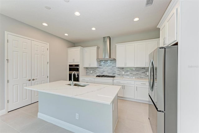 kitchen with stainless steel appliances, white cabinetry, sink, wall chimney exhaust hood, and a kitchen island with sink