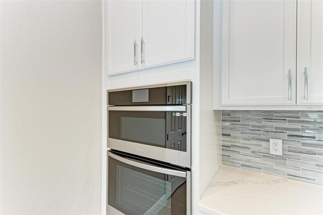 kitchen with stainless steel double oven, white cabinetry, light stone counters, and decorative backsplash