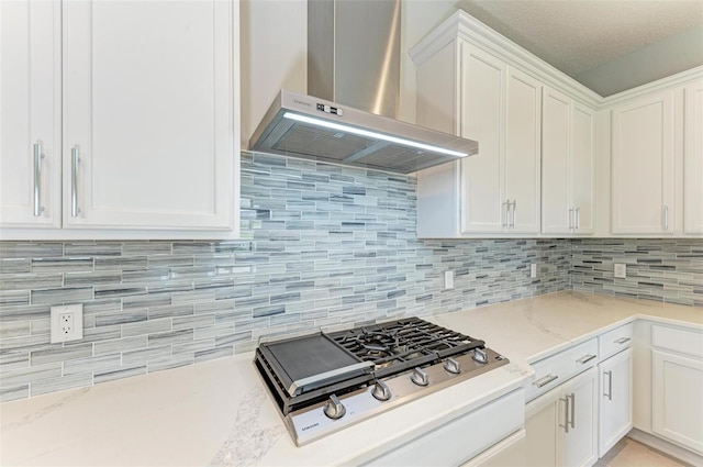 kitchen featuring white cabinets, light stone countertops, wall chimney range hood, and decorative backsplash