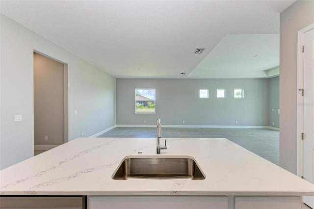 kitchen featuring light stone counters, sink, and an island with sink