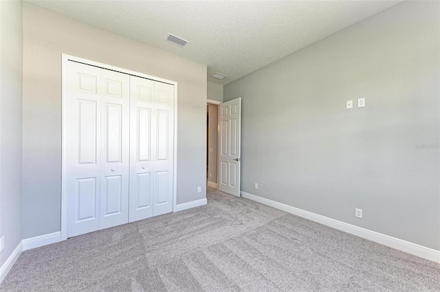 unfurnished bedroom with light carpet, a textured ceiling, and a closet