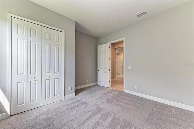 unfurnished bedroom with light colored carpet, a textured ceiling, and a closet