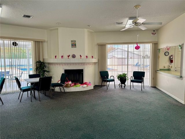 living area with carpet, a textured ceiling, ceiling fan, and a tiled fireplace