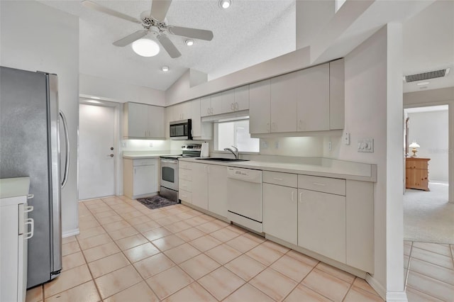 kitchen with sink, stainless steel appliances, a textured ceiling, lofted ceiling, and light tile patterned flooring