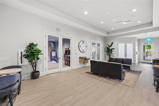 living room featuring french doors, light hardwood / wood-style floors, and a tray ceiling