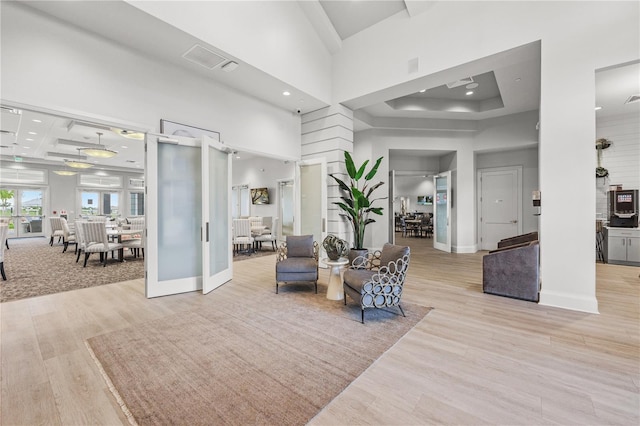 living area with coffered ceiling, french doors, a towering ceiling, a tray ceiling, and light hardwood / wood-style floors