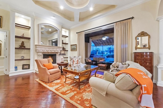 living room with built in features, ornamental molding, a warm lit fireplace, and hardwood / wood-style floors