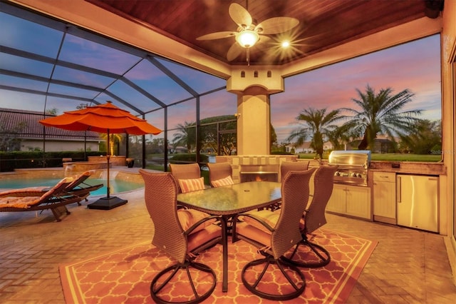 patio terrace at dusk with ceiling fan, area for grilling, and glass enclosure