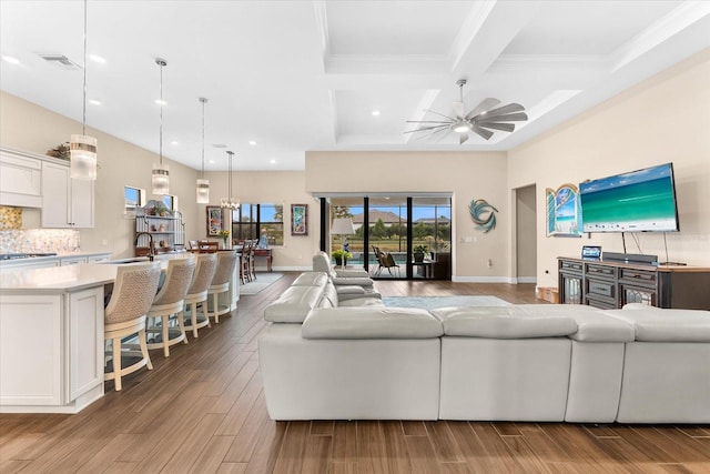 living room with light wood-type flooring, beam ceiling, coffered ceiling, sink, and ceiling fan with notable chandelier