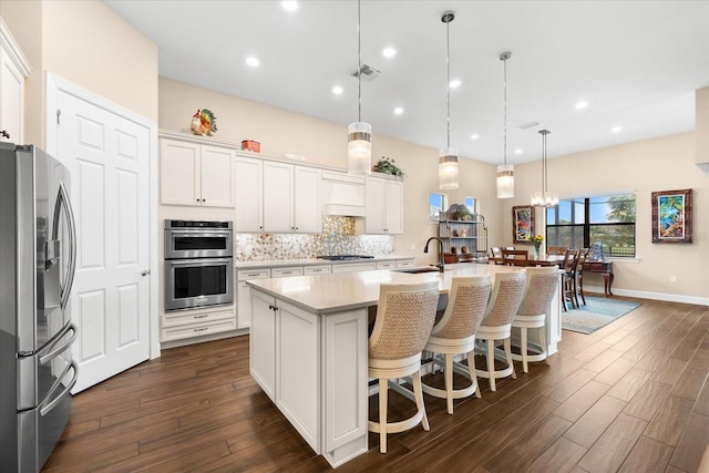 kitchen featuring a center island with sink, stainless steel appliances, decorative light fixtures, dark hardwood / wood-style flooring, and white cabinets