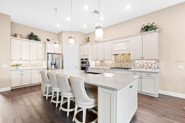 kitchen featuring a center island with sink, appliances with stainless steel finishes, dark hardwood / wood-style flooring, hanging light fixtures, and sink