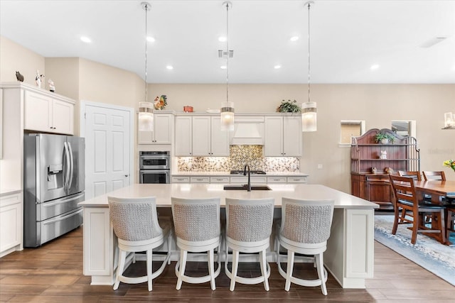 kitchen featuring an island with sink, premium range hood, decorative light fixtures, and appliances with stainless steel finishes