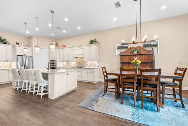 kitchen featuring dark hardwood / wood-style floors, pendant lighting, a center island with sink, and stainless steel appliances