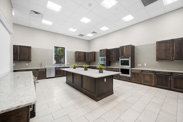 kitchen with appliances with stainless steel finishes, dark brown cabinetry, a high ceiling, and a kitchen island