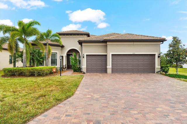 mediterranean / spanish home featuring a front yard, an attached garage, stucco siding, a tiled roof, and decorative driveway