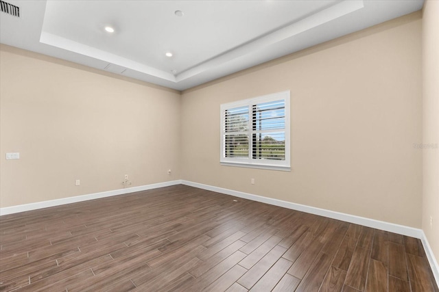 empty room with visible vents, baseboards, dark wood-type flooring, and a tray ceiling