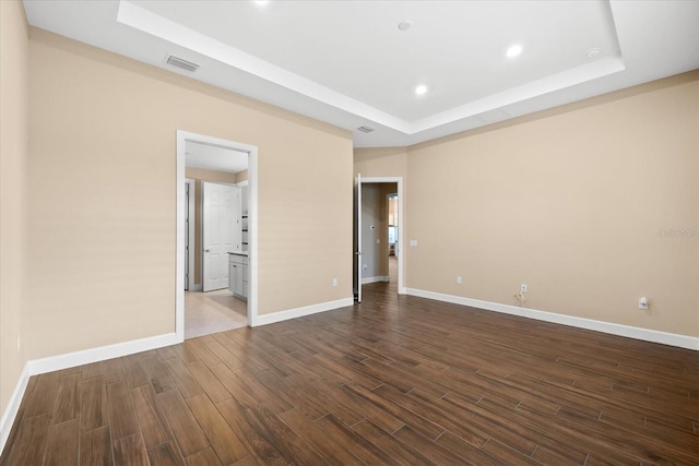 unfurnished bedroom with a tray ceiling, baseboards, and dark wood-style flooring