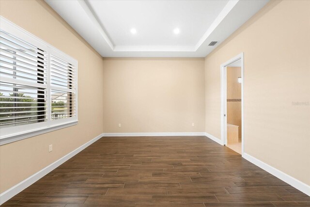 empty room featuring baseboards, visible vents, dark wood finished floors, recessed lighting, and a raised ceiling