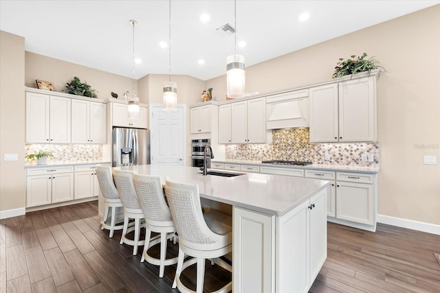 kitchen featuring custom exhaust hood, an island with sink, a sink, stainless steel appliances, and light countertops