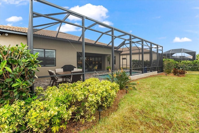 back of house with a patio, a yard, stucco siding, a tile roof, and a lanai