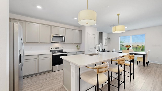 kitchen featuring appliances with stainless steel finishes, sink, gray cabinetry, hanging light fixtures, and a kitchen island with sink