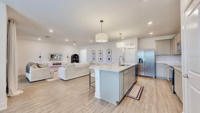 kitchen with sink, a center island with sink, a kitchen breakfast bar, pendant lighting, and stainless steel appliances