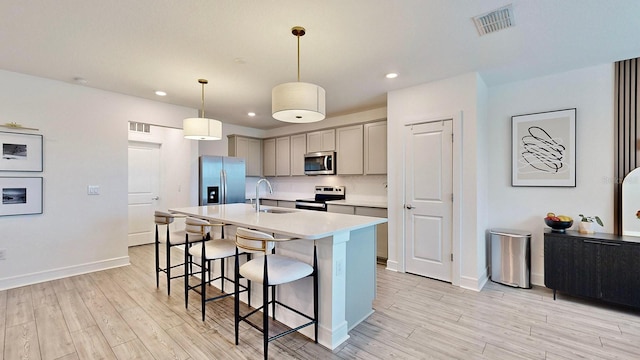 kitchen with sink, gray cabinets, pendant lighting, stainless steel appliances, and a kitchen island with sink