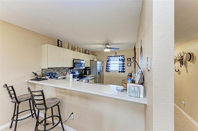 kitchen featuring stainless steel appliances, white cabinetry, backsplash, a kitchen breakfast bar, and kitchen peninsula