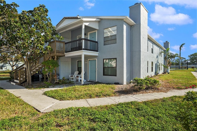 view of front of property featuring central air condition unit, a front lawn, a balcony, and a patio area