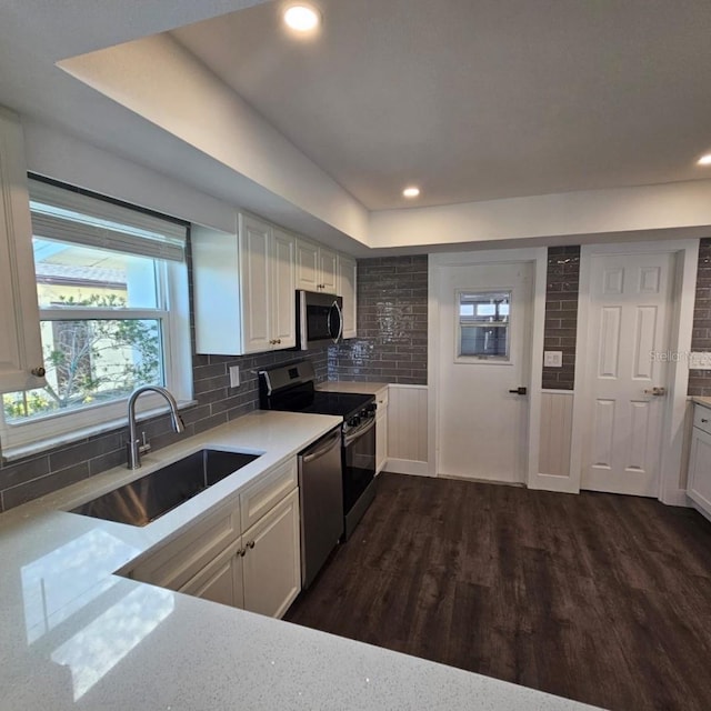 kitchen with dark wood-type flooring, sink, white cabinets, stainless steel appliances, and backsplash