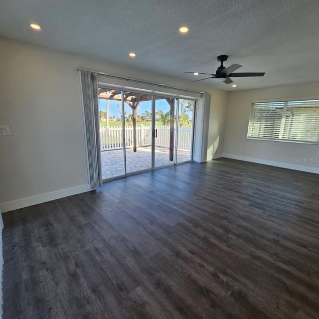 empty room featuring dark hardwood / wood-style flooring, ceiling fan, a wealth of natural light, and a textured ceiling