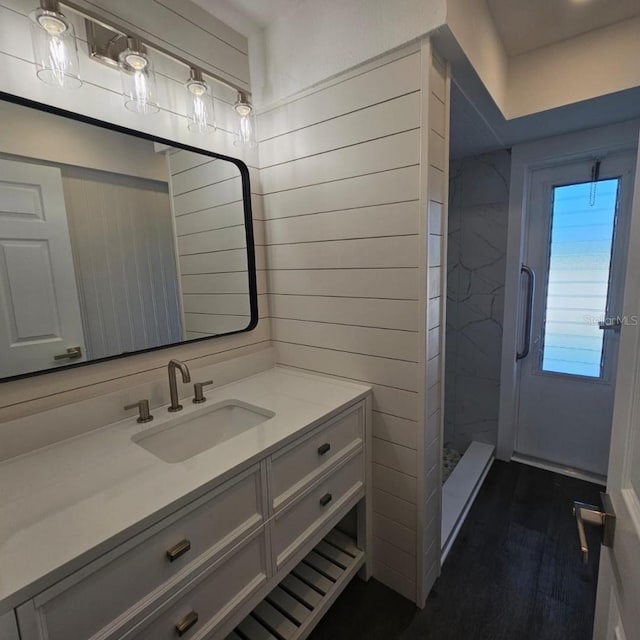 bathroom with tiled shower, vanity, and wood-type flooring