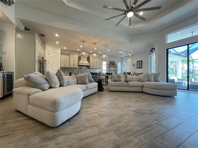 living room with ceiling fan with notable chandelier, a raised ceiling, a high ceiling, and wine cooler