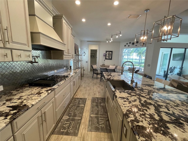 kitchen featuring light wood-type flooring, sink, decorative light fixtures, and custom exhaust hood