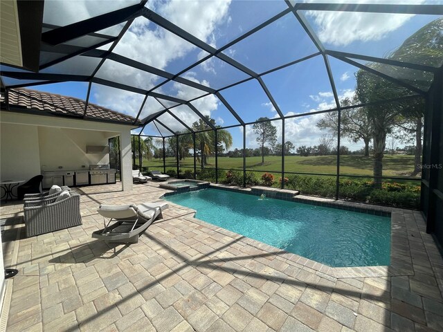 view of pool featuring an in ground hot tub, glass enclosure, a patio area, and exterior kitchen