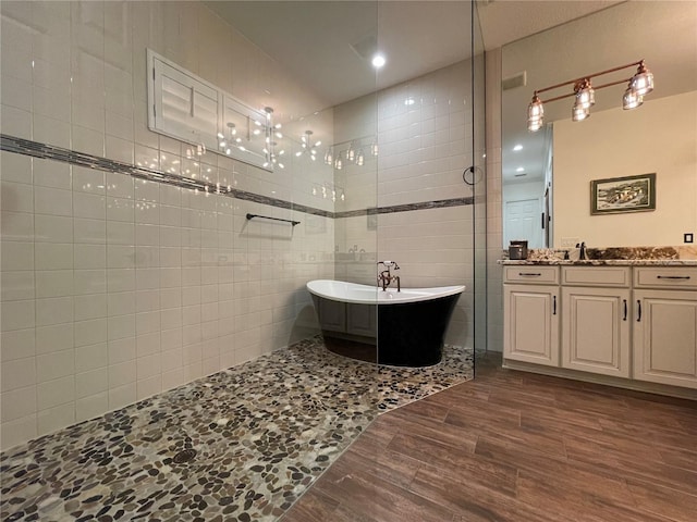 full bath with a walk in shower, wood finished floors, vanity, tile walls, and a freestanding bath