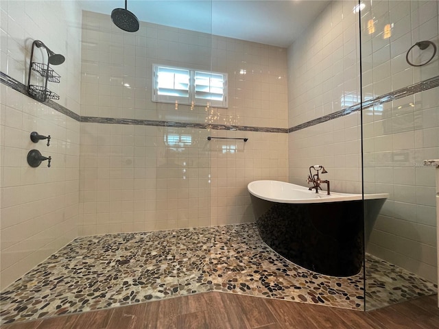 bathroom featuring a walk in shower, a freestanding tub, tile walls, and wood finished floors