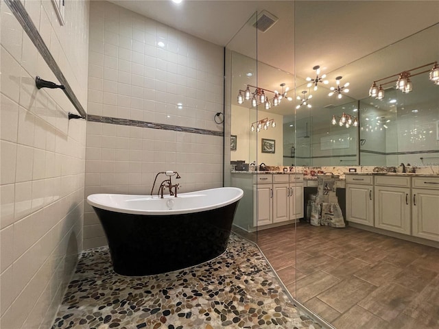 full bathroom with tile walls, a soaking tub, two vanities, visible vents, and a sink