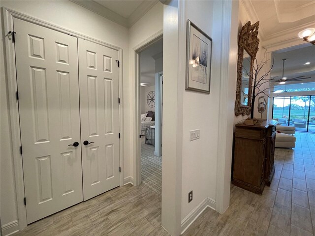 corridor featuring crown molding, light wood-style flooring, and baseboards