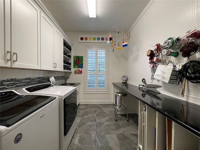washroom with a sink, cabinet space, washing machine and clothes dryer, a textured ceiling, and baseboards