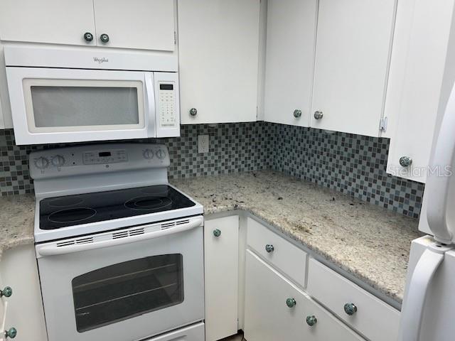 3751 S School Ave Unit 29, Sarasota, FL 34239 - kitchen featuring white appliances, white cabinetry, decorative backsplash, and light stone counters