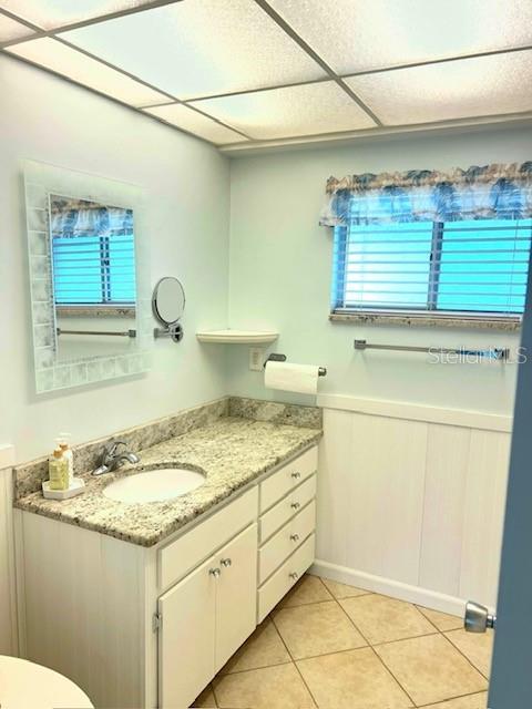 3751 S School Ave Unit 29, Sarasota, FL 34239 - bathroom with vanity, tile patterned floors, toilet, a paneled ceiling, and wainscoting