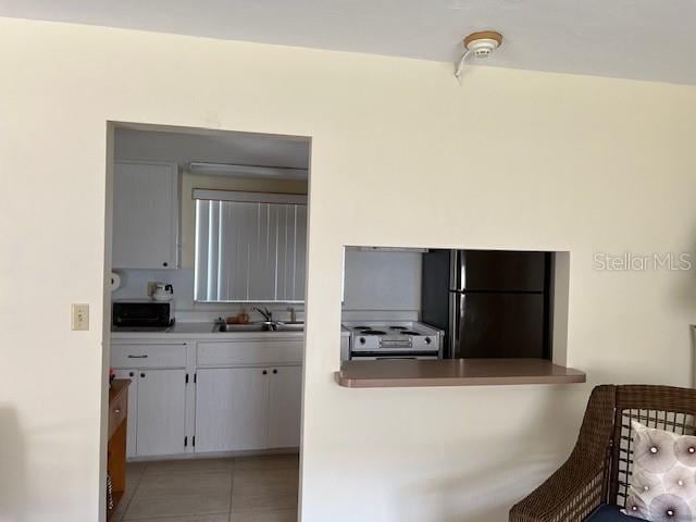 3751 S School Ave Unit 29, Sarasota, FL 34239 - kitchen featuring freestanding refrigerator, range with electric cooktop, light tile patterned flooring, a sink, and white cabinetry