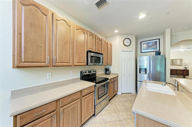 kitchen featuring appliances with stainless steel finishes, sink, light tile patterned floors, and a textured ceiling