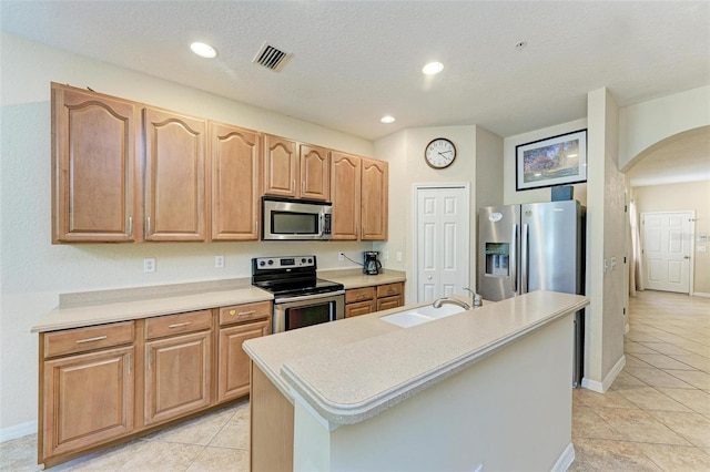 kitchen featuring appliances with stainless steel finishes, a textured ceiling, light tile patterned floors, sink, and a kitchen island with sink