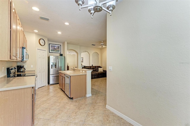 kitchen featuring stainless steel appliances, light brown cabinetry, a textured ceiling, light tile patterned floors, and an island with sink